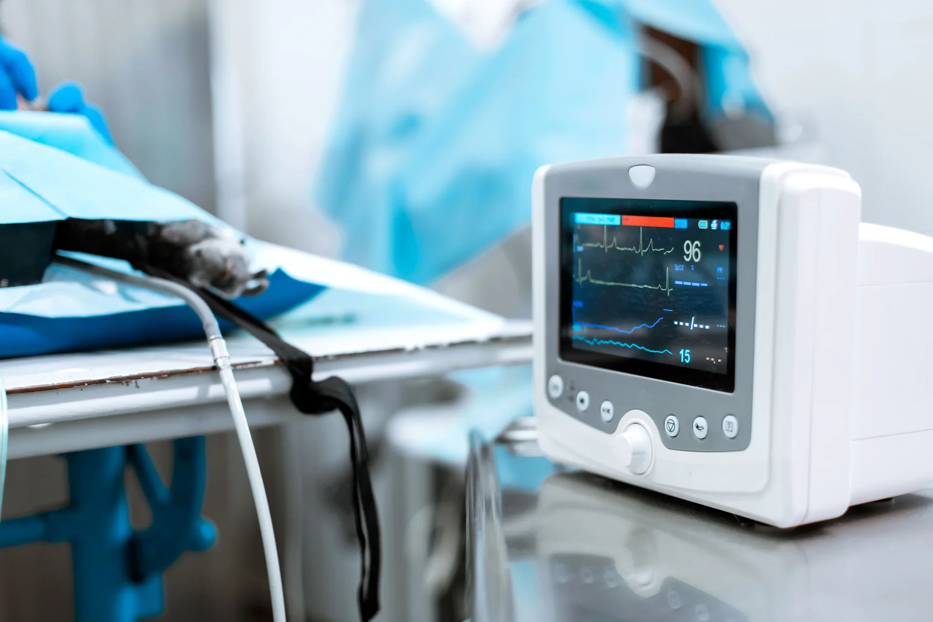 Medizinischer Vitalmonitor mit EKG-Kurve neben einem abgedeckten Behandlungstisch