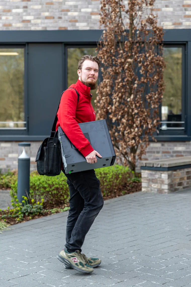 Nico Raufhake, Support & Technik bei medacom, in roter Jacke trägt einen schwarzen PC-Tower über den Vorplatz