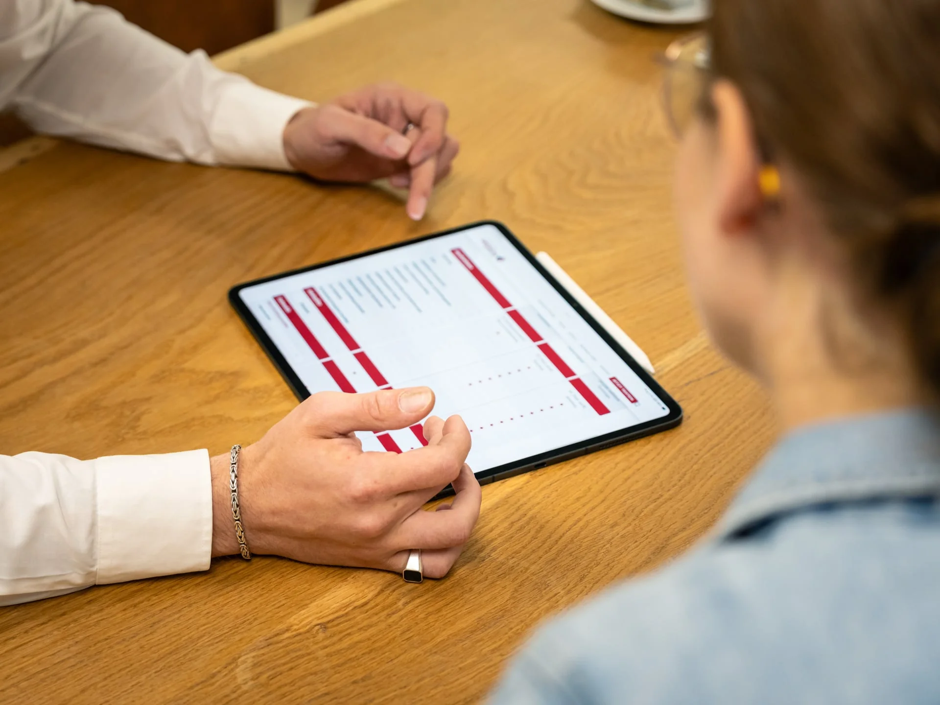 Zwei Personen am Tisch betrachten ein Tablet mit rot markiertem Dokument