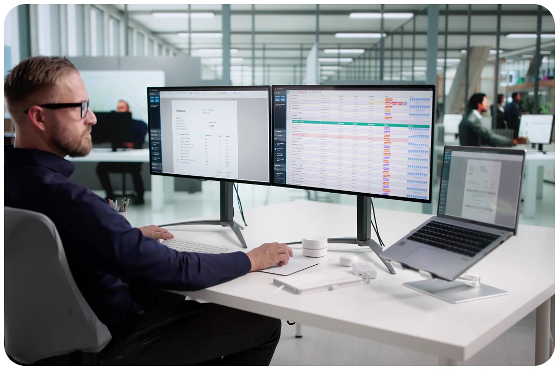 Mann mit Brille arbeitet im Büro an zwei Monitoren und Laptop mit Software