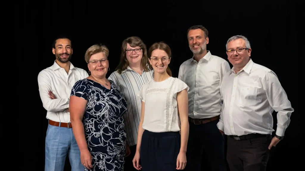 Sechs Personen des medacom-Teams im Gruppenporträt vor schwarzem Hintergrund