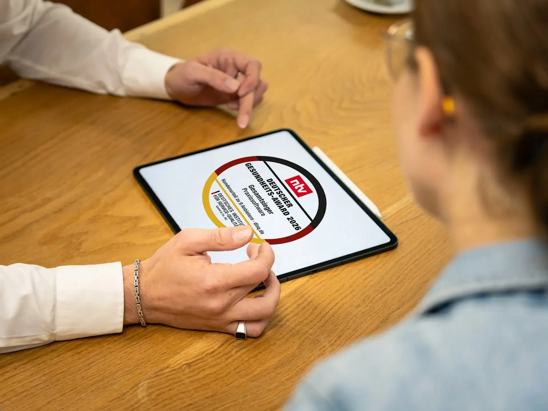 Zwei Personen am Tisch betrachten ein Tablet mit dem Siegel des Deutschen Gesundheits-Awards 2026 – Gesamtsieger Praxissoftware